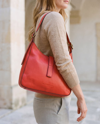 Person holding a red leather shoulder bag in a minimalistic setting