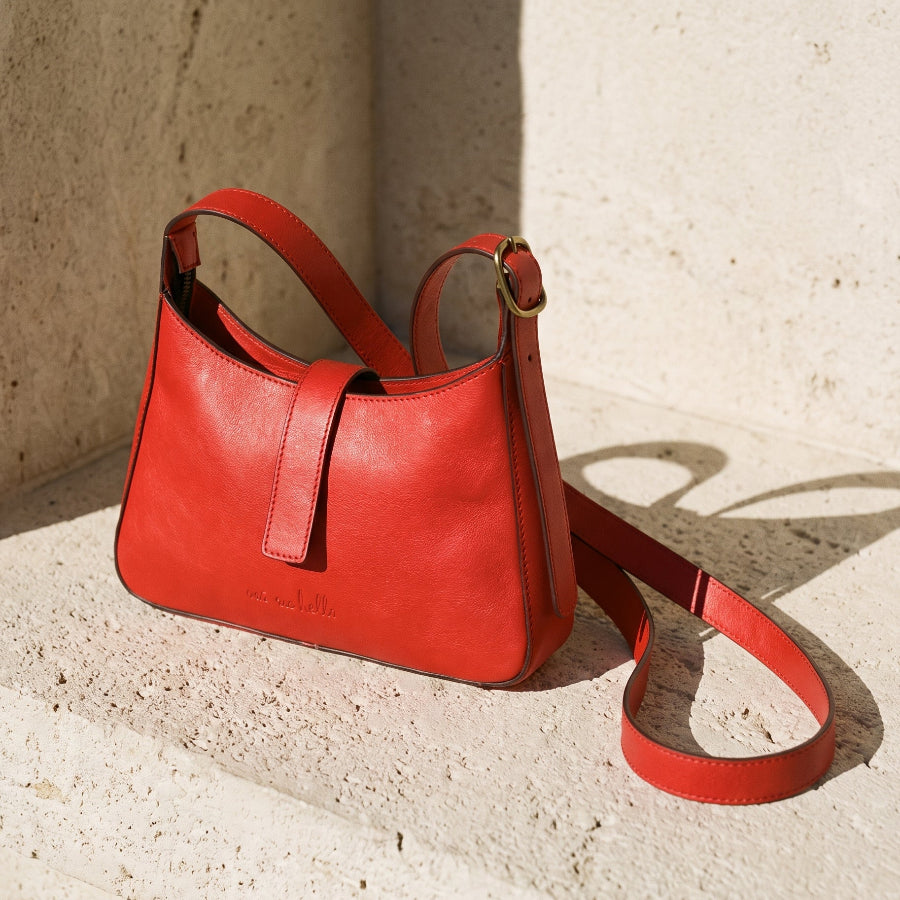 Red leather shoulder handbag with a strap on a textured beige surface