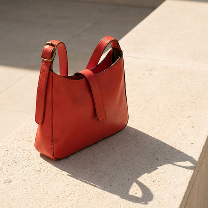 Red leather shoulder handbag with a strap on a textured beige surface