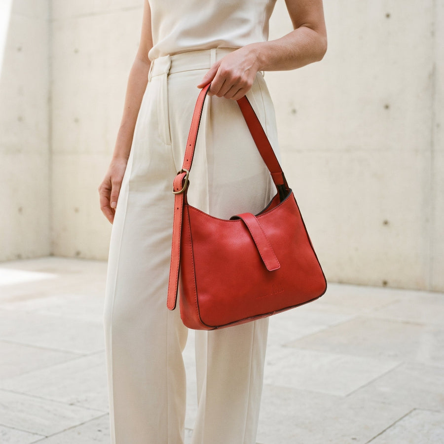 Person holding a red leather shoulder bag in a minimalistic setting