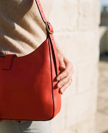 Close up a person holding a red leather shoulder bag in a minimalistic setting